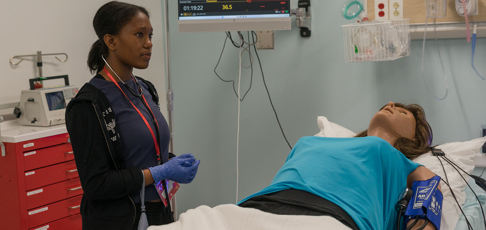 A medical student stands by the gurney of her practice model