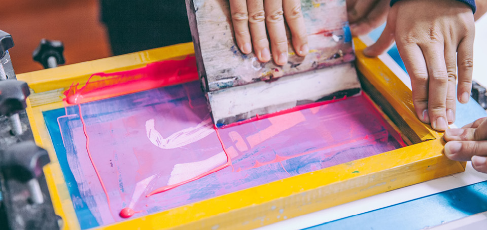 Student making a print on a piece of paper using pink ink.