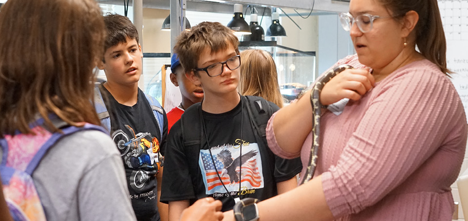 Teacher handling a snake while three students watch.